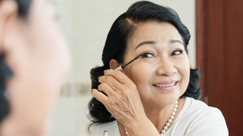 Femme plus âgée souriant tout en appliquant du mascara dans le miroir