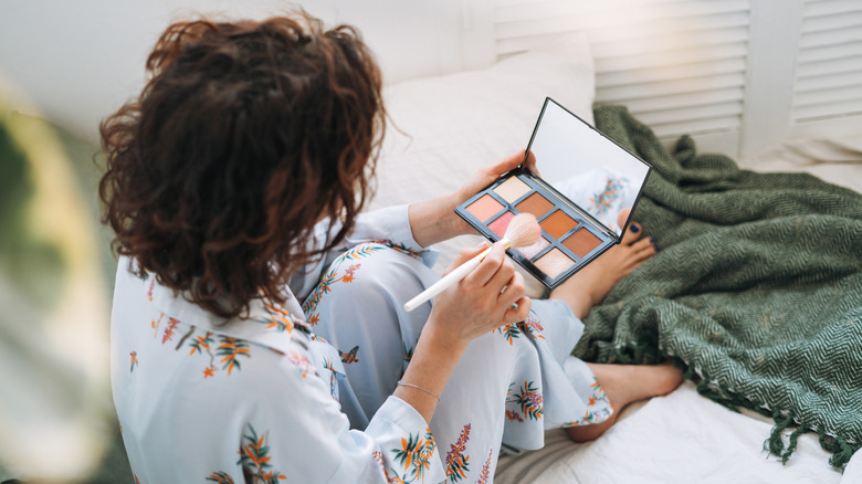 Sur l'épaule, instantané d'une femme brune en pyjama tenant une palette de modelage du visage