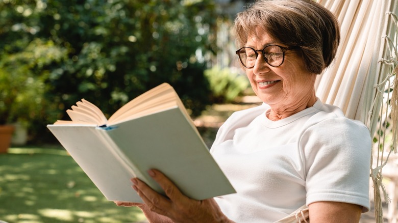 Femme âgée se détendant en lisant un livre dans un hamac à l'extérieur