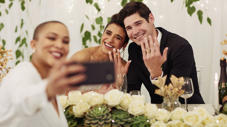 Couple de mariage montrant des signes de pièce et des lèvres de canard tout en tenant un téléphone pour un selfie