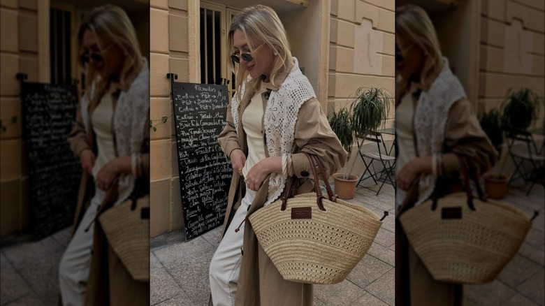 Une femme portant un sac en raphia avec une écharpe au crochet et un trench-coat