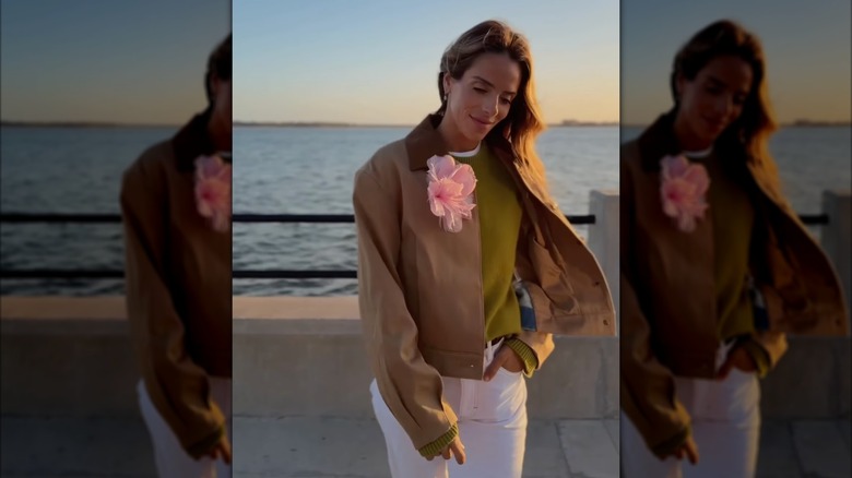 Une femme portant un manteau marron et un pantalon blanc avec une épingle à fleur rose