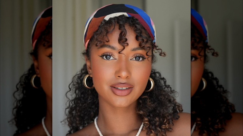 Une femme portant un foulard en soie autour de ses cheveux avec des cerceaux dorés et un collier