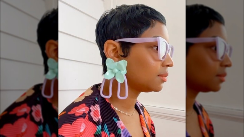 Une femme portant de grandes boucles d'oreilles bleues et violettes avec des lunettes violettes et une chemise brillante