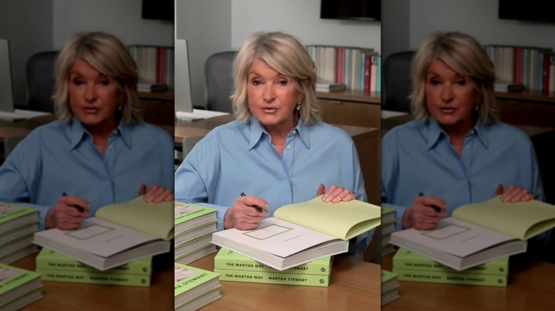 Martha Stewart assise à une table et signant une pile de livres