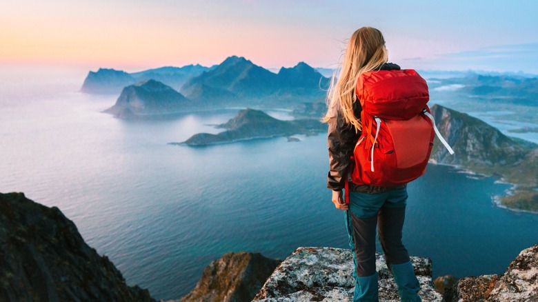Une femme seule regardant par-dessus une haute falaise portant un sac à dos rouge