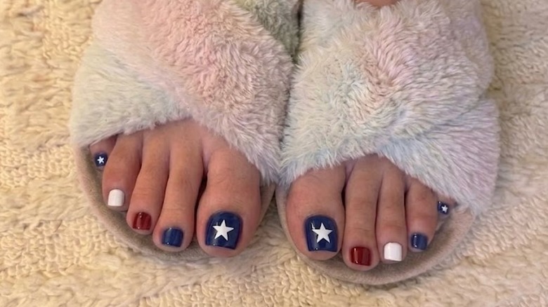 Une personne portant des pantoufles moelleuses avec une pédicure inspirée du drapeau américain