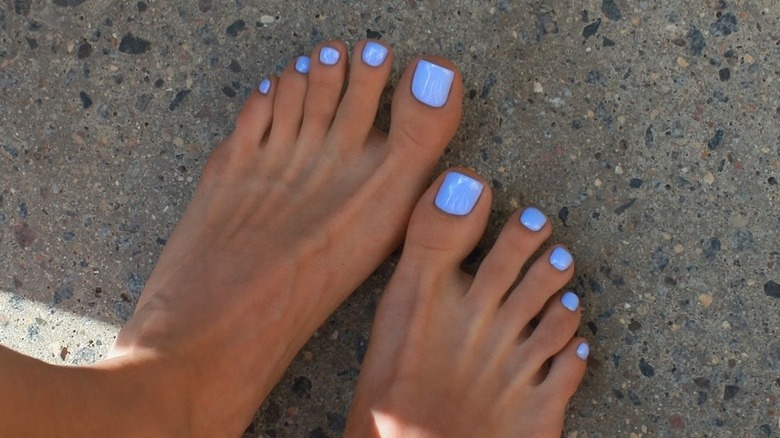 Une femme debout sur le sable avec une pédicure bleu ciel