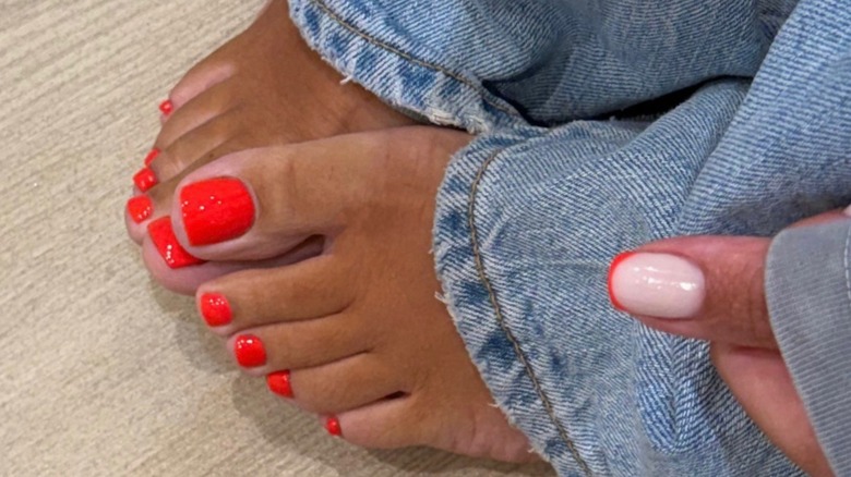 Une personne portant un jean bleu avec une pédicure rouge vif et brillante