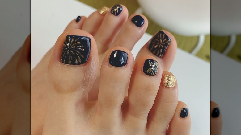 Une pédicure bleu marine foncé avec des paillettes dorées conçue pour ressembler à un feu d'artifice explosif