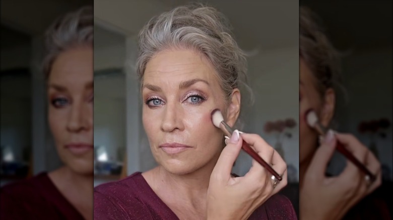 Une femme mélangeant du blush sur sa joue à l'aide d'un petit pinceau