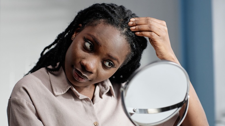 Une femme touchant ses cheveux dreadlocks en se regardant dans un miroir