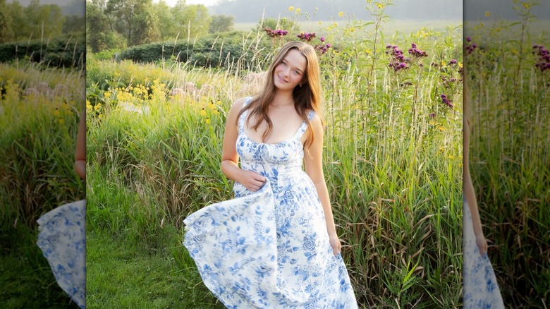 Une fille sourit dans un champ vêtue d’une robe à fleurs bleue et blanche