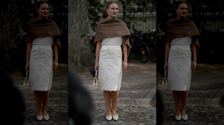 Une femme marche vêtue d'un trench-coat beige avec des gants en cuir noir