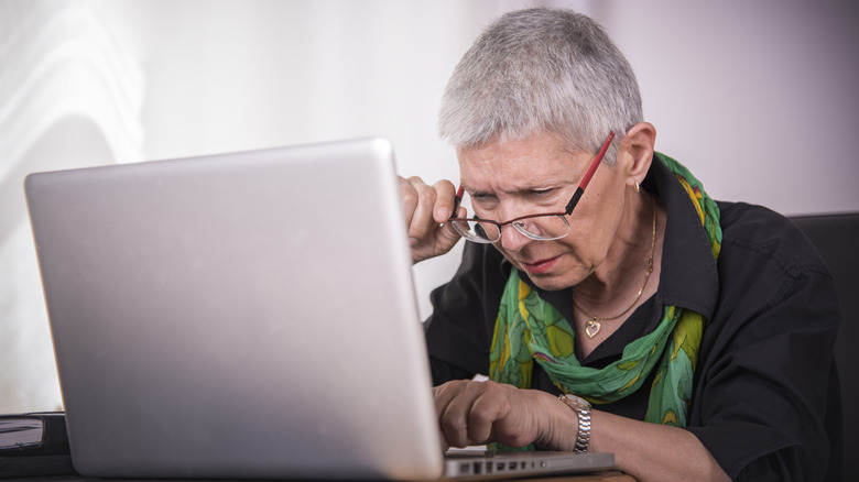 Une femme aux cheveux courts et aux lunettes utilisant un ordinateur portable et plissant les yeux