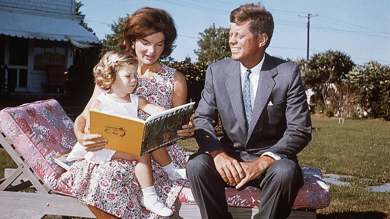 Jackie Kennedy avec son mari et sa fille lisant un livre dehors