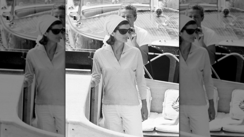 Jackie Kennedy en noir et blanc sur un bateau portant des lunettes de soleil et un foulard