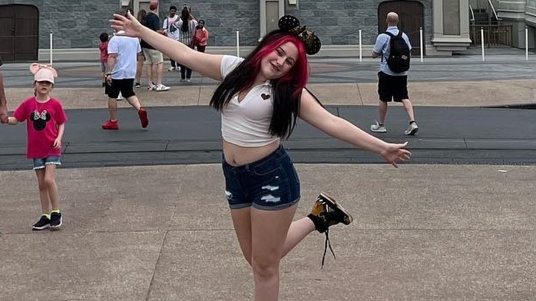 Bailee Ann DeFord posant à Disneyland dans un crop top et un short en jean aux cheveux noirs et roses