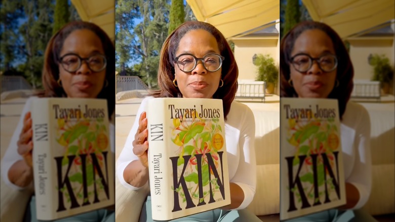 Oprah Winfrey brandissant un exemplaire de Kin en plein air