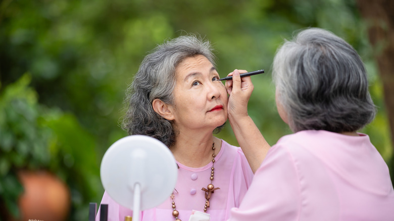 Femmes maquillant son amie, toutes deux portant des hauts roses