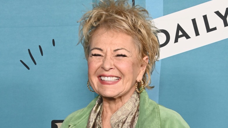 Roseanne Barr souriante sur le tapis rouge devant un fond bleu