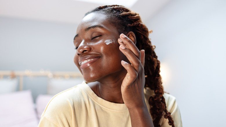 Une femme appliquant une lotion sur son visage en souriant