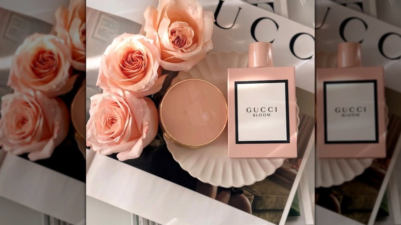 Parfum Gucci Bloom à plat aux côtés de fleurs et d'un miroir compact