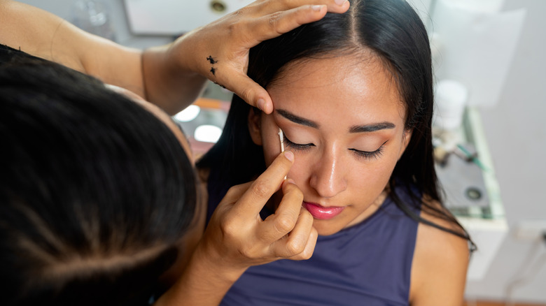 Maquilleuse appliquant un eye-liner sur les yeux d'une jeune femme avec un coton-tige