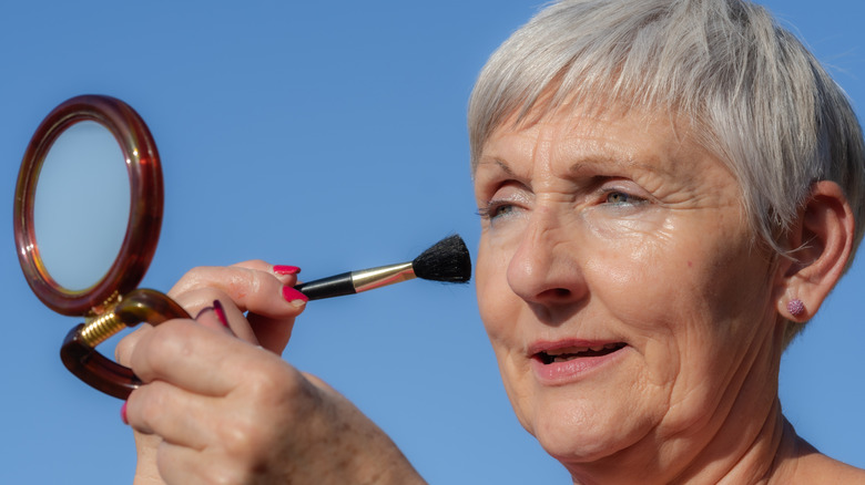 Femmes avec une coupe de lutin gris se maquillant dans un petit miroir