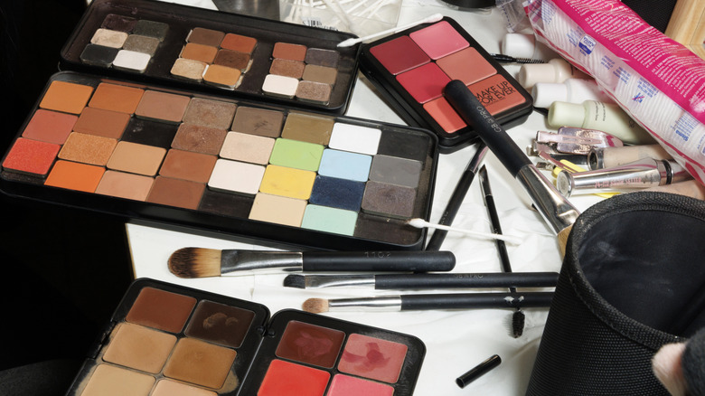 Divers pinceaux de maquillage posés à plat avec trois palettes cosmétiques de couleurs de maquillage