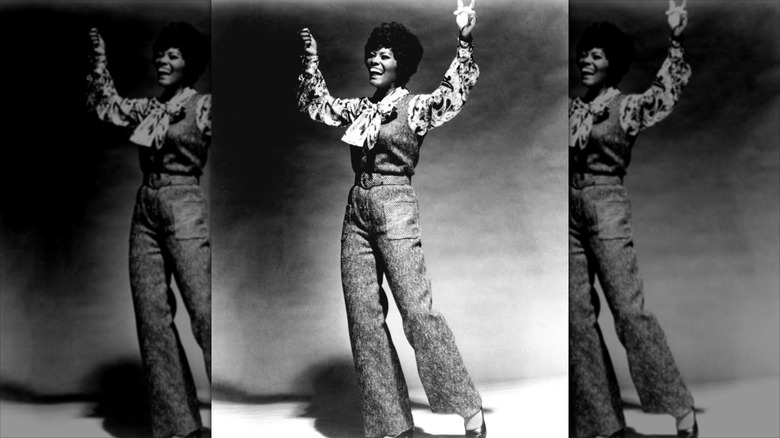 Dionne Warwick lève les mains en l'air avec un pantalon évasé taille haute