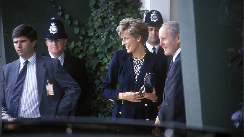 La princesse Diana marche et porte un blazer noir avec des boutons dorés