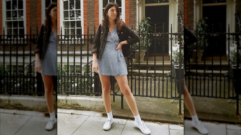 Une femme vêtue d'une robe courte et d'une veste marron à l'extérieur portant des Keds