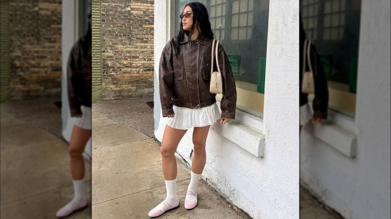 Une femme vêtue d'un manteau en cuir avec une jupe blanche et des baskets de ballet roses