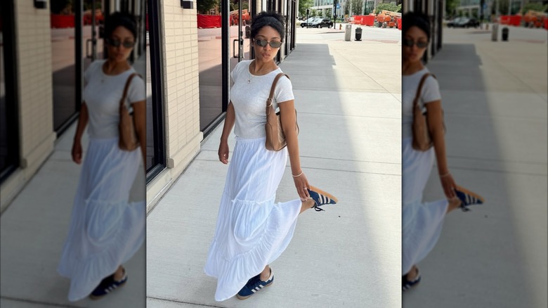 Une femme vêtue d'une jupe et d'une chemise blanches avec des baskets Adidas bleues