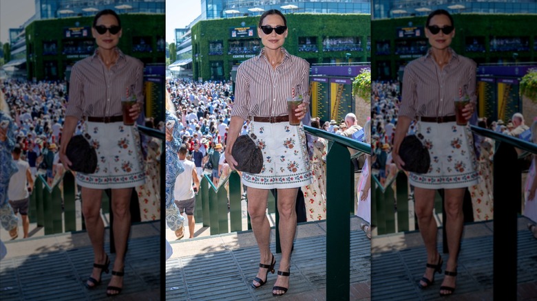 Minnie Driver portant une chemise boutonnée rayée, un short à motifs et tenant un cocktail
