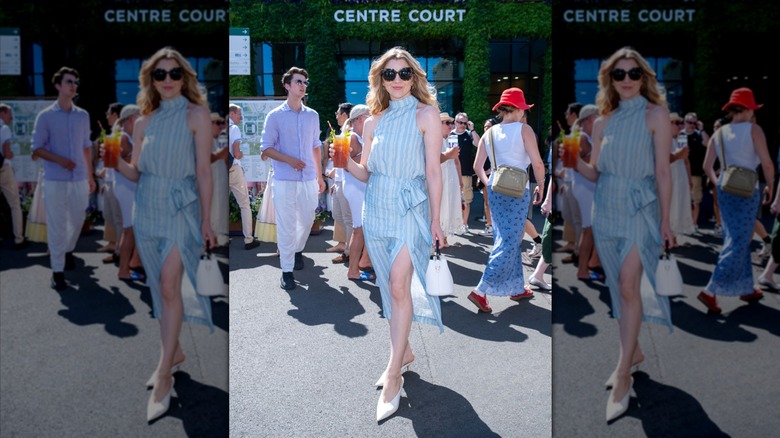 Natalie Dormer porte des lunettes de soleil et une robe dos nu bleue tout en tenant un cocktail