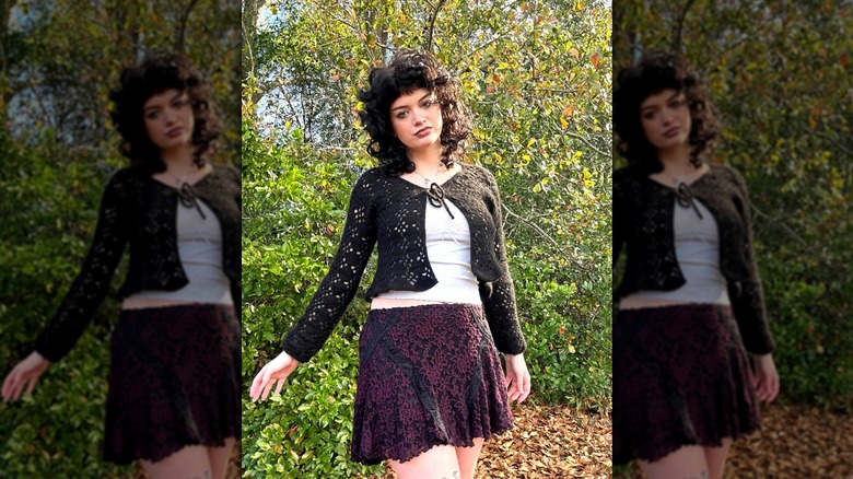 Une femme debout à l’extérieur, vêtue d’une mini-jupe et portant un cardigan noir à tissage ouvert
