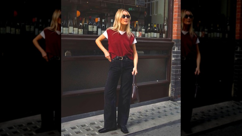Une femme debout dans la rue en vert noir et un gilet pull rouge