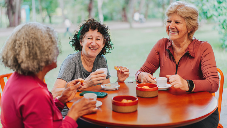 Trois femmes âgées partageant une collation et un expresso autour d'une table