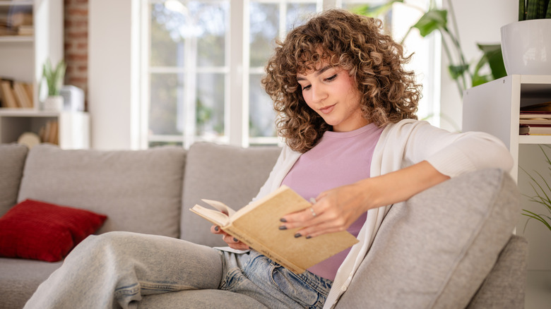 Une jeune femme aime lire tout en se relaxant sur un canapé confortable à la maison, entourée d'un décor chaleureux et de la lumière naturelle provenant de grandes fenêtres