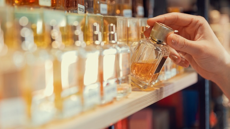 La main d'une femme prend du parfum sur une étagère dans un magasin