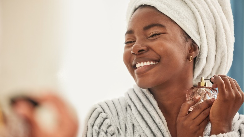 Une femme souriante vaporisant du parfum sur son cou