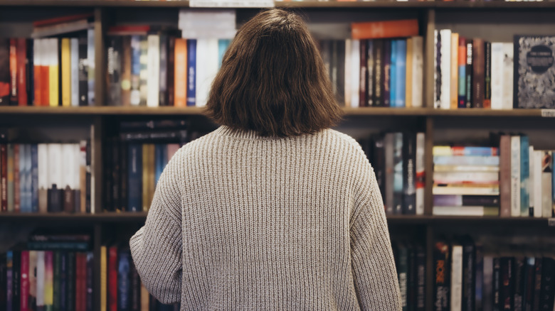 Jeune femme brune choisissant un livre dans une librairie, vue arrière