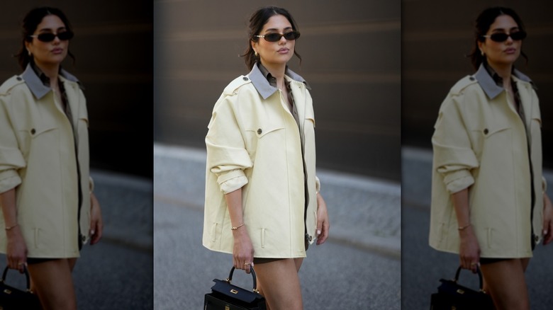 Femme en veste jaune beurre et sac noir avec lunettes de soleil ovales