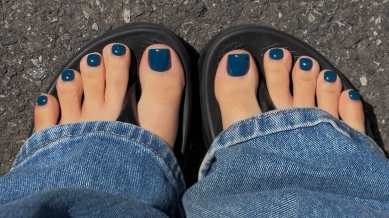Une femme portant un jean bleu et des sandales noires avec une pédicure bleu foncé