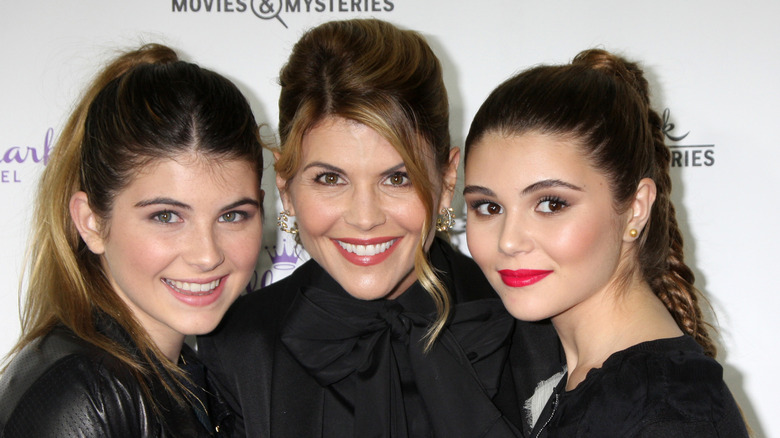 Lori Loughlin porte un haut noir à nœud papillon et un chignon avec des reflets blonds.