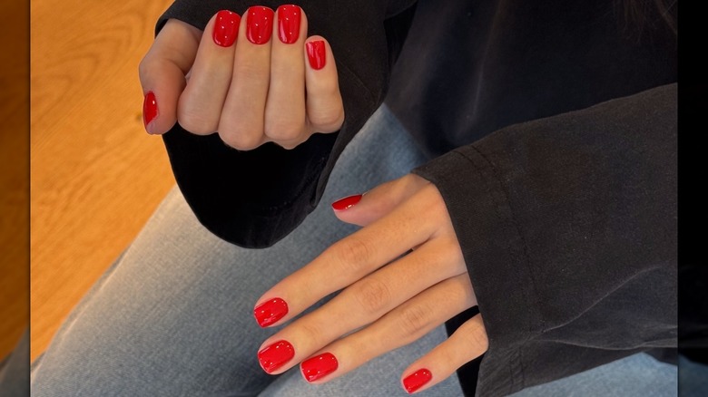 Les mains d'une femme montrant sa manucure courte et rouge tout en portant un haut noir et un jean bleu
