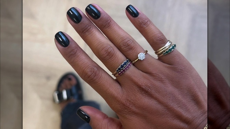 La main d'une femme avec plusieurs anneaux montrant sa manucure courte et noire