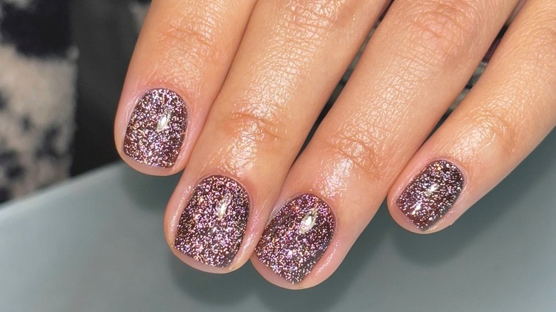 La main d'une femme montrant sa manucure à paillettes brunes sur des ongles courts